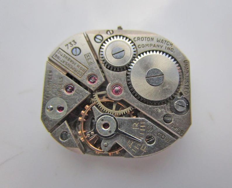May include: A detailed view of a vintage Croton watch movement. The silver mechanism displays various gears, jewels, and the text "CROTON WATCH COMPANY INC." and "SEVENTEEN JEWELS". The watch movement is non-magnetic and Swiss made.