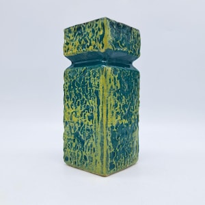 May include: A textured, rectangular ceramic vase in shades of teal and yellow. The vase has a unique, rough surface and a geometric shape with a square top and base. The color palette is a mix of teal and yellow.