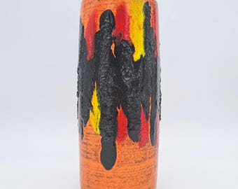 May include: A cylindrical orange ceramic vase with a textured black, red, and yellow design. The vase has a rough, dripped paint effect, creating a unique and artistic appearance. The vase is a decorative item.