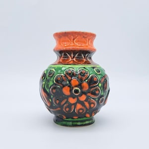 Op de afbeelding: Een keramieken vaas met een bolvormig lichaam en een uitlopende hals. Het oppervlak is versierd met een reliëfpatroon van gestileerde bloemen in levendig oranje, diepzwart en heldergroen glazuur voor een textuurrijk en kleurrijk uiterlijk.