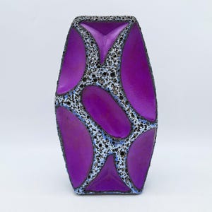 May include: A decorative vase with a unique design. The vase features a vibrant purple color with a pattern of oval shapes. The spaces between the ovals are filled with a speckled, textured material, creating a striking contrast.