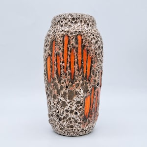 May include: A cylindrical ceramic vase with a textured, porous surface. The vase has vertical orange stripes against a brown and white background. The vase is a decorative item.