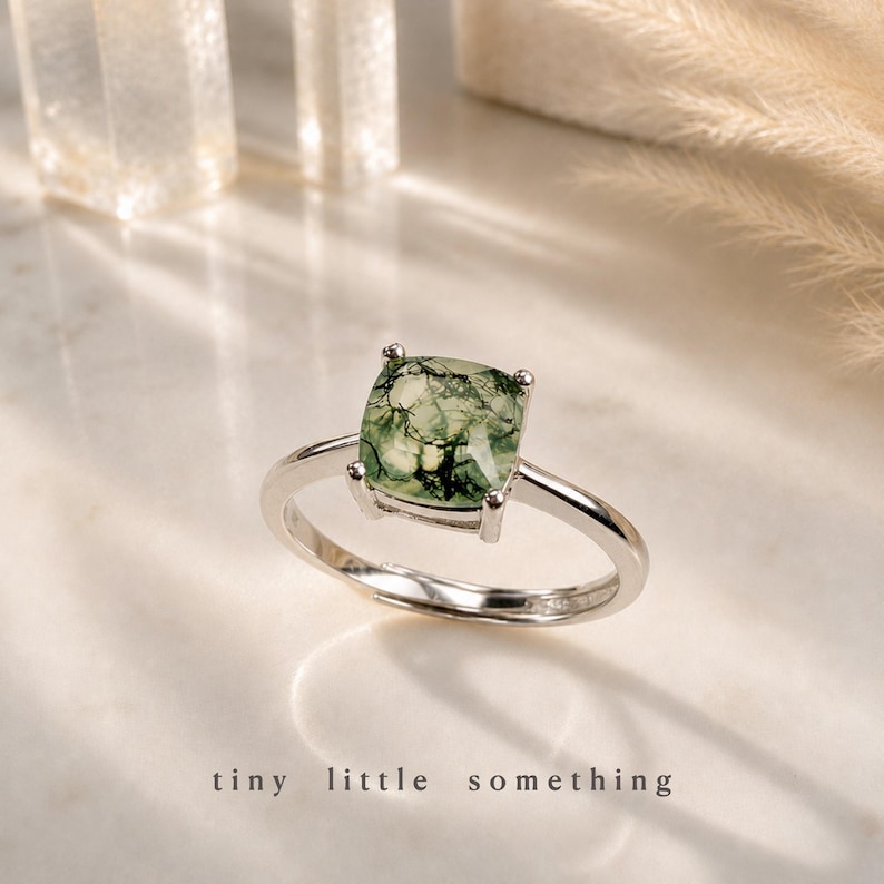 Puede incluir: Un anillo de plata con una piedra de &aacute;gata musgosa verde cuadrada. La piedra tiene un patr&oacute;n natural &uacute;nico. El anillo est&aacute; sobre una superficie blanca con las palabras "tiny little something" en la parte inferior.