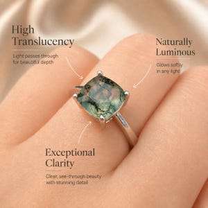 Puede incluir: Un anillo de plata con una piedra preciosa de &aacute;gata musgosa de corte cuadrado. La piedra muestra inclusiones verdes y marrones, con el texto "High Translucency", "Naturally Luminous" y "Exceptional Clarity". El anillo se muestra en un dedo.
