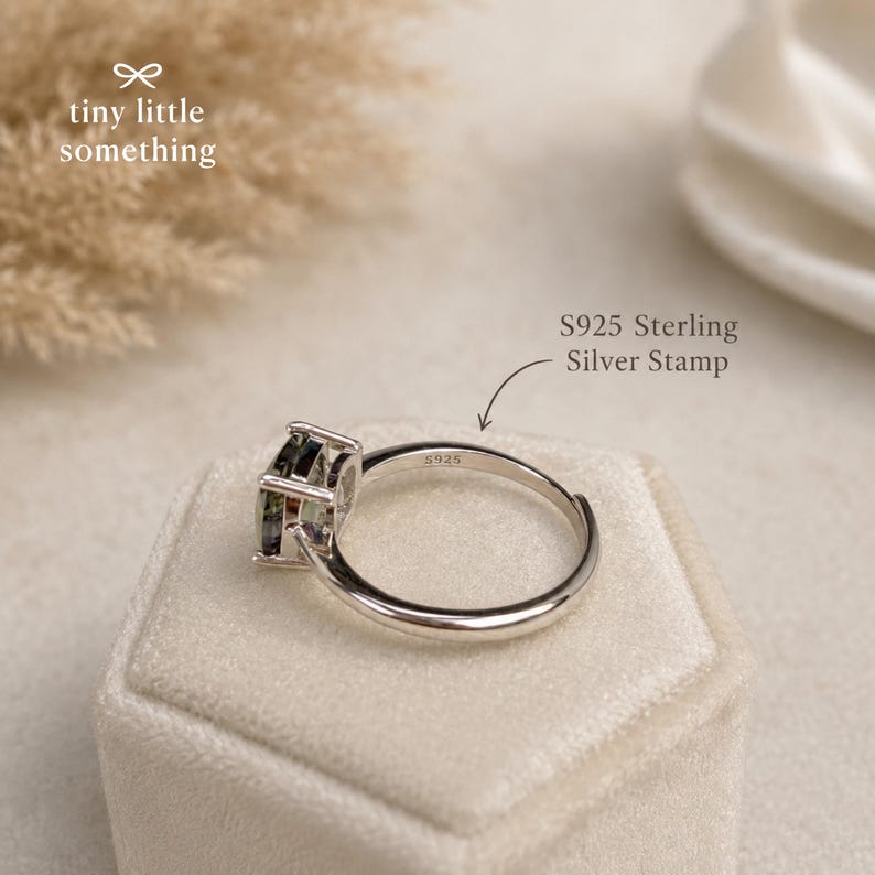 Puede incluir: Un anillo de plata de ley con una gema cuadrada y multicolor. El anillo est&aacute; estampado con "S925" y se muestra sobre una superficie suave y clara. El anillo es de "tiny little something".