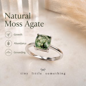 Puede incluir: Anillo de plata con una gema de &aacute;gata musgosa natural de corte cuadrado, con inclusiones verdes y blancas. El texto "Natural Moss Agate" y "tiny little something" est&aacute; presente.