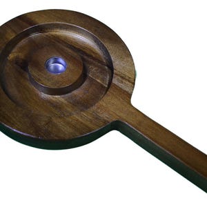 May include: A wooden handheld tool with a round, concave surface and a handle. The tool has a small, round hole in the center of the concave surface.