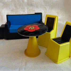 May include: A black and yellow plastic dollhouse furniture set with a blue couch, two chairs, and a table with a red flower design.
