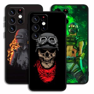 May include: Three black phone cases with unique designs. One features a figure in a helmet with flames, another a skull wearing a helmet and red scarf, and the third a character in a green and black outfit.
