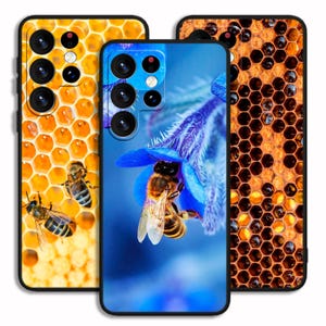 May include: Three phone cases with bee-themed designs. One case features a honeycomb pattern with bees, another showcases a bee on a blue flower, and the third displays a honeycomb pattern. The cases have black borders.