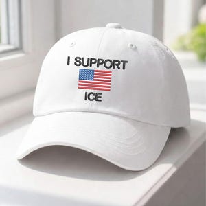 May include: White baseball cap featuring the embroidered text "I SUPPORT ICE" in black, above a depiction of the American flag. The cap has a curved peak and a button on top.
