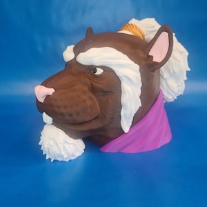 May include: A 3D-printed sculpture of a brown rat's head with white fur accents and a pink nose and ears. The rat wears a purple scarf and has a rope tied around its head. The sculpture is set against a blue background.