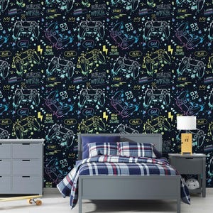 Könnte beinhalten: Ein Schlafzimmer mit einem Bett mit einer blau karierten Bettdecke und Kissen. Die Tapete hat ein sich wiederholendes Muster aus bunten Videospiel-Controllern, Texten und Grafiken auf einem dunkelblauen Hintergrund. Eine graue Kommode und ein Nachttisch sind ebenfalls zu sehen.