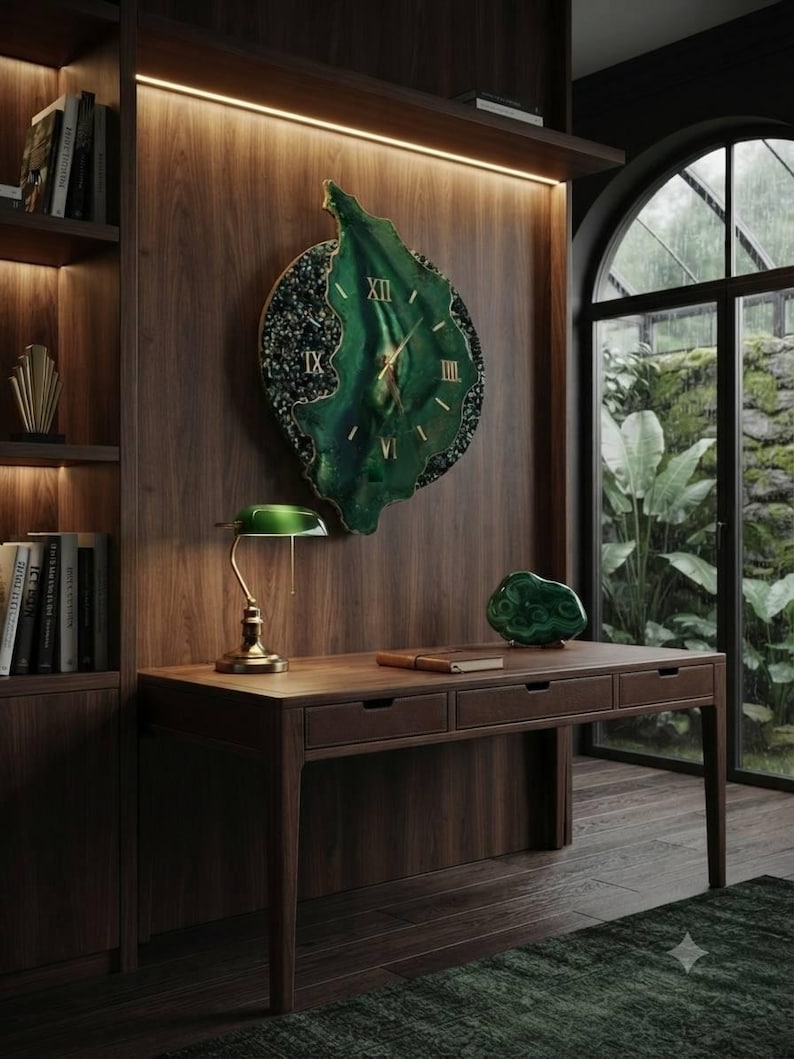 May include: A large, irregular, green wall clock with gold Roman numerals and hands, featuring a textured, dark, speckled border. The clock is mounted on a dark wood paneled wall above a wooden desk with three drawers, a green lamp, and a green stone.