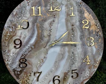 May include: Round wall clock with a marbled design in shades of white, brown, and gray. The clock face features gold-colored numerals and hands. Decorative elements include small, sparkling accents.