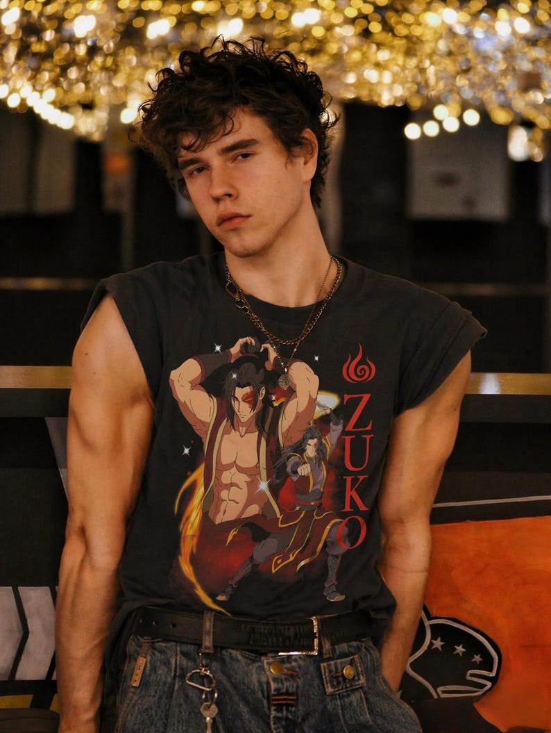 May include: Dark gray sleeveless t-shirt featuring a graphic of a character with the word "Zuko" in red. The person is wearing a gold chain necklace, blue jeans, and a black belt.
