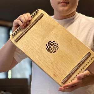 May include: A wooden musical instrument with strings and a decorative design in the centre. The instrument is being held by a person's hands.