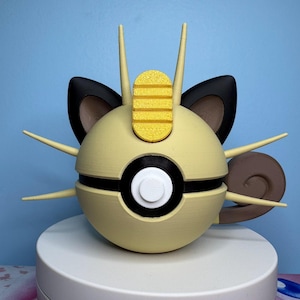 May include: A 3D printed figurine of a Pokemon character,  Persian, with a yellow and black Pokeball design. The figurine is beige, black, brown, and yellow.