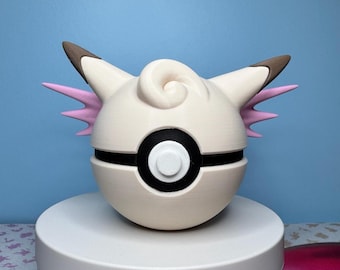 May include: A cream-colored, spherical object with black and white details, resembling a Poké Ball. It features a swirl on top, pink wing-like accents, and brown-tipped ears. The object is displayed on a white pedestal against a blue background.