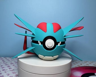 May include: A 3D-printed, stylized sculpture of a blue and red creature with wing-like appendages. The sculpture has a round body with a black and white circular design in the center. The creature is displayed on a white, circular stand against a blue background.