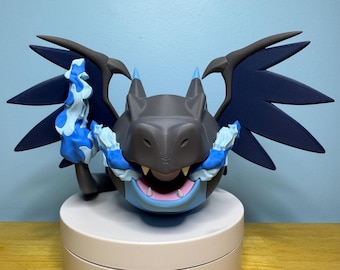 May include: A 3D-printed dragon figurine in grey, blue, and white. The dragon has large, dark blue wings, blue accents, and a light blue underbelly. It is posed on a white circular base.