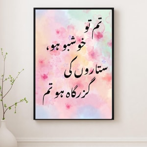 以下が含まれることがあります： ピンク、パープル、ブルーの背景の水彩画。絵画には、アラビア語で「人生で最も美しいものは、物ではなく瞬間である」と書かれた黒い書道の引用が描かれています。