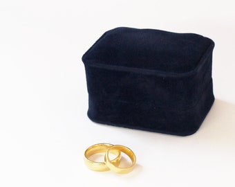 May include: Two gold wedding bands in a blue velvet ring box.