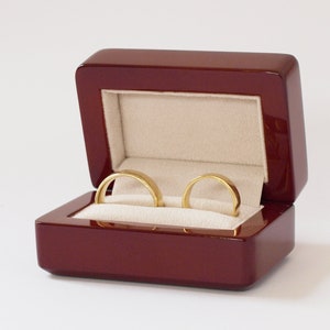 May include: Two gold wedding bands in a dark red wooden ring box with a cream colored interior.
