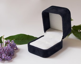 May include: A dark blue velvet ring box with a white velvet interior. The box is open and the lid is folded back.