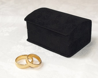 May include: Two gold wedding bands in a black velvet ring box.