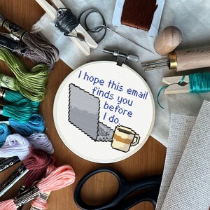 Może przedstawiać: Obręcz do haftu krzyżykowego z napisem "I hope this email finds you before I do." Projekt zawiera pikselowy laptop i filiżankę kawy. Wok&oacute;ł obręczy znajdują się nici do haftu i narzędzia.
