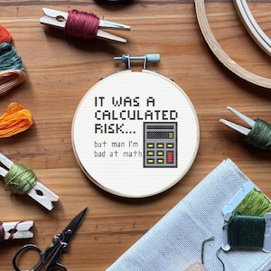 Peut inclure: Un cercle de broderie au point de croix avec le texte "IT WAS A CALCULATED RISK... but man I'm bad at math" et un graphique de calculatrice. La broderie est dans un cercle en bois, entourée de fournitures de broderie.