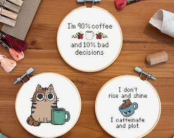 May include: Three cross-stitch hoops with humorous coffee-themed quotes. One says "I'm 90% coffee and 10% bad decisions." Another features a cat with a mug. The third says "I don't rise and shine, I caffeinate and plot."