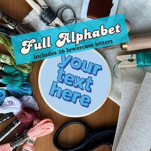 May include: A blue embroidery hoop with the text "your text here" in blue thread. The hoop is surrounded by embroidery floss, scissors, and a wooden needle minder. The text "Full Alphabet includes 26 lowercase letters" is in a blue banner above the hoop.
