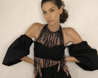 Puede incluir: Conjunto negro de dos piezas con top halter con flecos y mangas caídas, combinado con una falda a juego. El conjunto lo lleva una persona con cabello oscuro.
