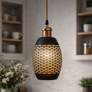 May include: Black pendant light with a copper-colored top and a patterned, perforated design. The light hangs from a brown cord, illuminating a kitchen setting. The light fixture has a unique, modern aesthetic.