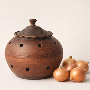 May include: A brown ceramic onion keeper with a lid, featuring decorative leaf patterns and ventilation holes. Several onions are placed next to the keeper. The keeper is approximately 7 inches in diameter.