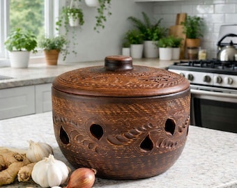 May include: A round, dark brown clay garlic keeper with a matching lid. The vessel features a textured, carved surface with decorative leaf patterns and several teardrop-shaped ventilation holes around the sides to allow for airflow.