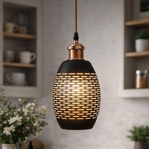 May include: A matte black pendant light with a cylindrical shape featuring horizontal cutouts that allow light to pass through. The fixture includes a metallic copper-colored top cap and is suspended by a brown cord from the ceiling.