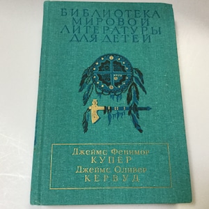 Könnte beinhalten: Ein türkisfarbenes Buch mit goldener Schrift und einem von amerikanischen Ureinwohnern inspirierten Design. Der Buchtitel ist auf Russisch, und der Name des Autors ist ebenfalls auf Russisch. Das Cover zeigt ein dekoratives Emblem mit Federn und einem Tomahawk.