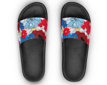 May include: Pair of black slide sandals with a floral pattern. The straps feature a design of red, blue, and white flowers on a white background. The sandals have a textured sole.