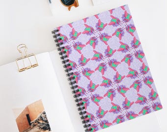 Puede incluir: Un cuaderno con espiral con un patrón repetido de formas abstractas y coloridas sobre un fondo lavanda. El diseño presenta elementos rosas, verdes y morados. El cuaderno está abierto sobre una superficie blanca, con un clip dorado y gafas de sol visibles.