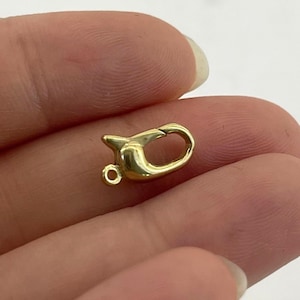 Puede incluir: Un pequeño cierre de langosta dorado. El cierre tiene un cuerpo redondeado con una palanca con resorte y un pequeño lazo para sujetarlo a una cadena u otro componente de joyería. El cierre está diseñado para sujetar joyas de forma segura.