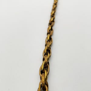 Op de afbeelding: Close-up van een goudkleurige ketting met ovale schakels. De ketting heeft een getextureerd oppervlak en staat tegen een witte achtergrond. De ketting maakt waarschijnlijk deel uit van een ketting of armband.