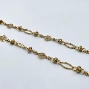 Puede incluir: Primer plano de dos collares dorados. Cada collar presenta una delicada cadena con eslabones ovalados y en forma de trébol alternados, intercalados con pequeños detalles de cuentas. Los collares se muestran sobre un fondo blanco.