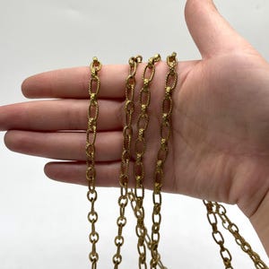 May include: Several strands of gold-colored chain with oval and rope-like links. The chains are displayed against a neutral background. The chains are likely for jewelry making or crafting.