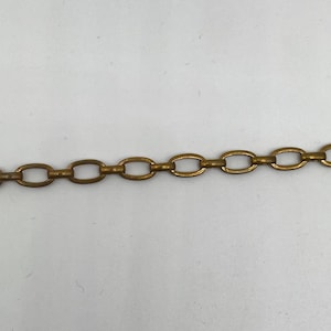 May include: Close-up of a section of a gold-colored chain. The chain links are oval-shaped and connected in a linear pattern. The chain has a slightly aged appearance, suggesting it may be vintage or antique.