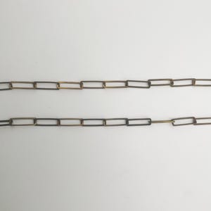 May include: Two parallel chains with rectangular links. The links have a two-tone color scheme, with a dark outer edge and a lighter, possibly gold-toned, inner section. The chains are set against a plain white background.