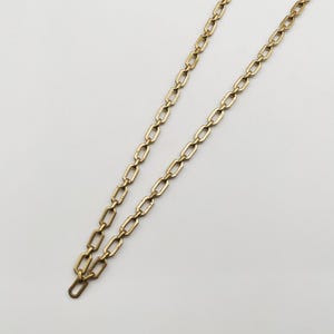 Op de afbeelding: Een goudkleurige ketting met rechthoekige schakels. De ketting wordt gepresenteerd tegen een witte achtergrond, waarbij het ontwerp en de kleur worden getoond. Het is een sieraad.