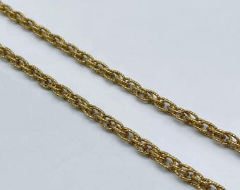 Könnte beinhalten: Nahaufnahme von zwei goldfarbenen Kettenhalsketten. Die Ketten haben ein strukturiertes, gewebtes Design. Der Hintergrund ist eine schlichte weiße Oberfläche. Die Ketten sind im Bild schräg angeordnet.